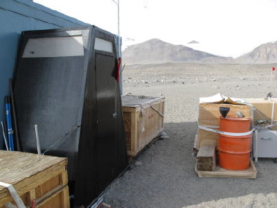 The outhouse (black structure) and urine drum (orange drum with a funnel) at camp.